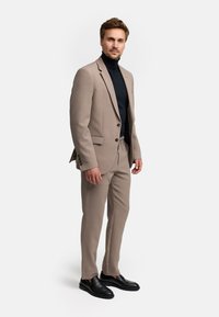 Beige kostuum met een getailleerde blazer en tapered broeken, gecombineerd met een zwarte coltrui. Afgemaakt met zwarte instappers voor een elegante uitstraling.