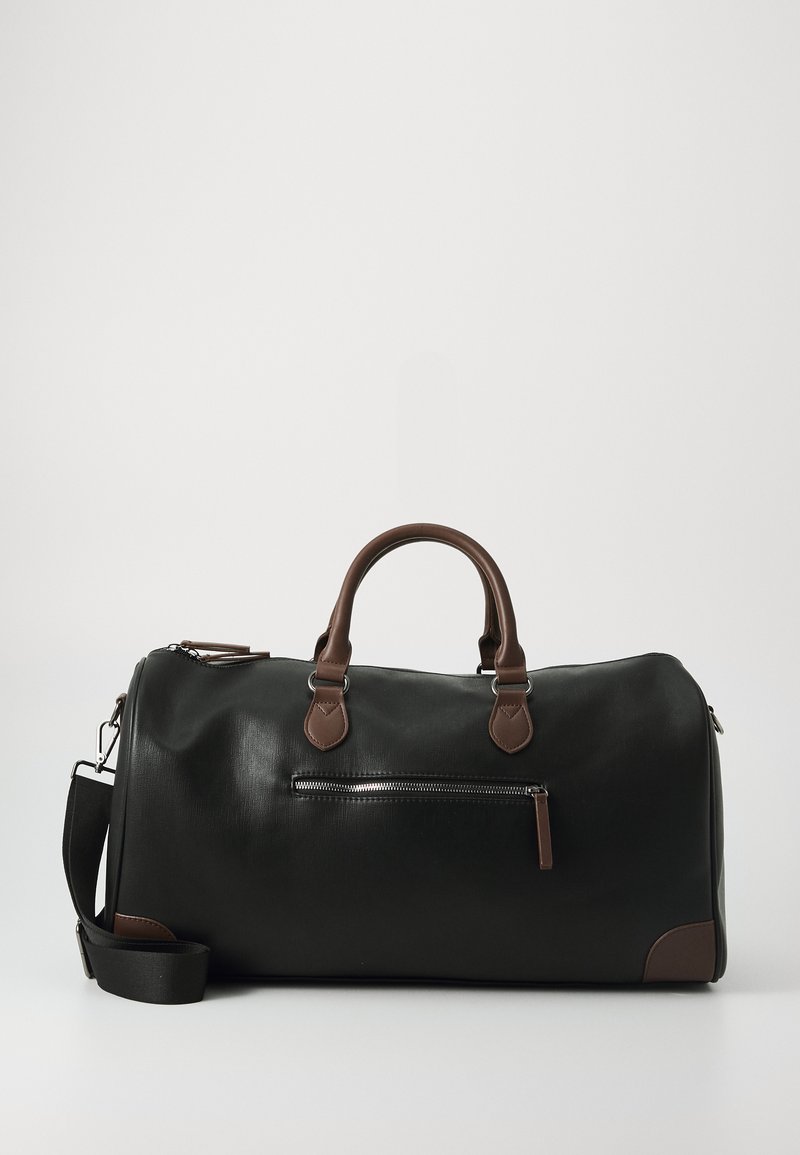 Bolso de viaje de cuero negro con detalles marrones, que cuenta con dos asas, una correa para el hombro ajustable y un bolsillo frontal con cremallera.