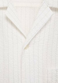 Witte pyjamashirt met een subtiele gewatteerde textuur, verticale grijze strepen, een notch-kraag en een enkele knoopsluiting. Beschikt over een borstzak.