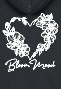 Felpa nera con cappuccio caratterizzata da un design grafico bianco di un cuore composto da fiori, accompagnato dal testo "Bloom Mood" in un carattere corsivo in basso.