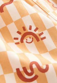 Oranžovo-krémová kostkovaná látka s grafikou slunce s usměvavou tváří a vlnitými liniemi v tmavě oranžové barvě. Hladká textura.