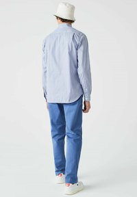 Camisa de manga larga a rayas azul y blanca combinada con pantalones de mezclilla azul claro y zapatillas blancas. La camisa tiene un cuello clásico y puños abotonados.