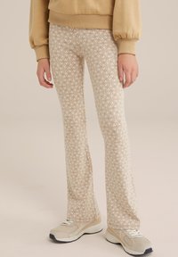 Pflare pletene hlače v svetlo bež barvi z belim cvetličnim vzorcem. Obute z bež supergami, ki imajo teksturirano tkanino in prilega zasnovo.