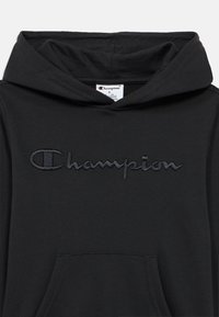 Μαύρο φούτερ με κουκούλα και εσωτερική τσέπη τύπου καγκουρό στο μπροστινό μέρος, με κεντημένο λογότυπο "Champion" σε πιο σκούρο τόνο. Κατασκευασμένο από μαλακό, υφασμάτινο ύφασμα με υφή.
