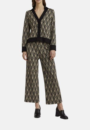 Donna che indossa un cardigan beige e nero con motivo geometrico abbinato a pantaloni a gamba larga e mocassini neri con tacco a blocco.