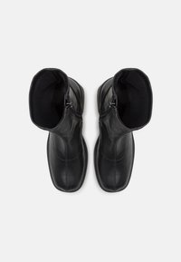 Paire de bottines en cuir noir avec fermetures éclair latérales, bouts carrés arrondis et doublure intérieure douce, vues de dessus sur un fond blanc.