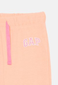 Ferskenfargede joggebukser med rosa snøring og hvit "GAP" logo. Mykt stoff med en jevn tekstur og elastisk midje.