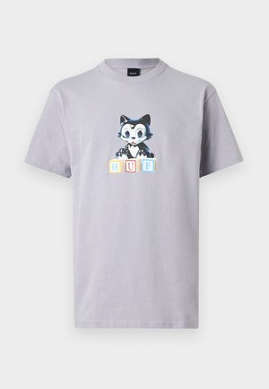 Hallikas puuvillane T-särk, millel on trükitud joonistus kassist suurte silmadega, istub värviliste plokkide kõrval, millel on kirjas "HUF." Ümmargune kaelus, lühikesed varrukad.