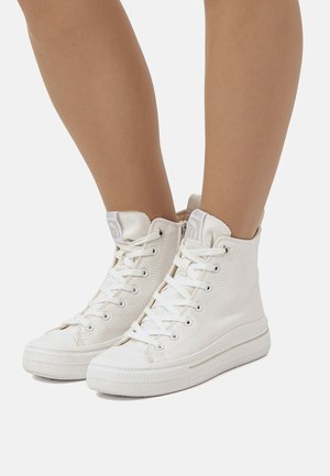 Sneaker alte bianche in tela con lacci bianchi, suole in gomma e un'etichetta con logo sulla parte superiore. Presentano una superficie in tessuto testurizzato e un design classico.