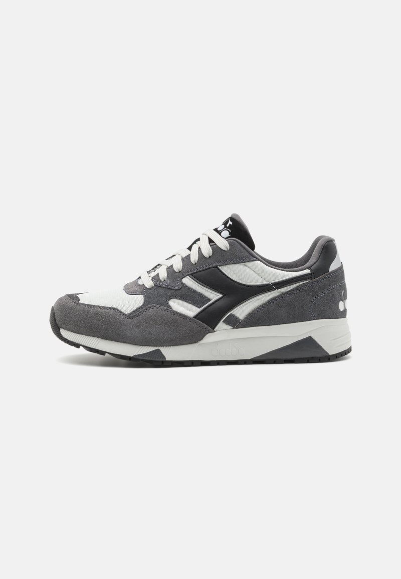Gray and white athletic sneaker with suede and mesh materials, featuring a black logo, white laces, and a patterned sole.