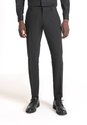 Pantaloni neri su misura con fronte piatto, vestibilità slim e texture liscia, abbinati a scarpe eleganti nere.