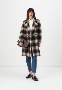 Wollmischung, zweireihiger Mantel im schwarz-beigen Karomuster; oversized Passform mit Reverskragen, kombiniert mit einem weißen Hemd und Jeans.