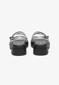 Sandalias de tiras plateadas con una suela de plataforma negra, que cuentan con una correa trasera y un acabado suave y brillante en el material superior.