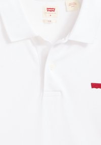 White polo shirt made of cotton, featuring a two-button placket, ribbed collar, and red embroidered Levi's logo on the left chest.