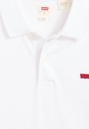Vit pikétröja i bomull, med en knappslå med två knappar, ribbad krage och röd broderad Levi's-logga på vänster bröst.