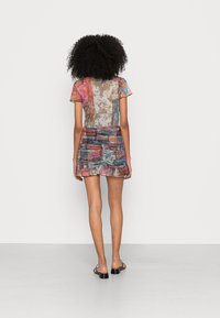 Haut transparent avec des motifs floraux dans des tons de rose, bleu et orange, associé à une mini-jupe multicolore froncée. Des sandales plates noires complètent le look.
