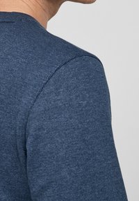 Suéter de punto azul marino con un acabado texturizado. Presenta un cuello redondo y costuras visibles a lo largo de los hombros y el cuello.