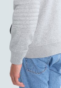 Gray sweatshirt with ribbed texture on the sleeves, paired with light blue denim jeans. Focus on sleeve detailing and fabric composition.