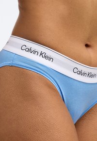 Ανοιχτό μπλε βαμβακερό εσώρουχο με λευκή ζώνη μέσης που φέρει το λογότυπο "Calvin Klein" σε μαύρο. Λεία υφή με εφαρμοστή σχεδίαση.