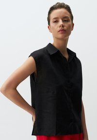 Camicia in lino nera con colletto, design senza maniche e chiusura a bottoni frontale. Presenta spacchi laterali per una vestibilità rilassata.