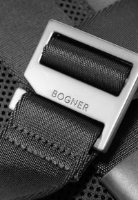 Cinturino nero in nylon con fibbia metallica d'argento incisa con la scritta "BOGNER." Presenta un motivo testurizzato, bordi lisci e dettagli di cucitura sicuri.