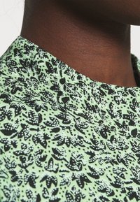 Mintgrön tyg med ett svart abstrakt mönster, med en strukturerad krage och mjuk textur, närbild av halsområdet.