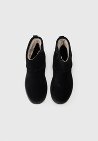 Botas negras hasta el tobillo de ante con un forro suave, que presentan una superficie lisa, forma redondeada y una lengüeta en la parte posterior para facilitar su colocación.