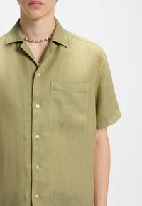Lichtgroen shirt met korte mouwen van een textuurstof, voorzien van een knoopsluiting aan de voorkant en een enkele borstzak met een zachte, ontspannen pasvorm.