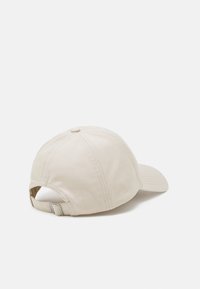 Beige bomulls baseballhette med buet skjerm, justerbar stropp bak og en knapp på toppen. Glatt tekstur og sydd detaljer.