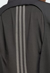 Black jacket with textured fabric and smooth contrasting back. Features three vertical lines of circular patterns in light gray.