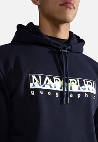 Donkerblauwe hoodie met een voorlogo in het wit en multikleur, voorzien van een trekkoord in de capuchon en een zachte textuur. Casual fit met een grafisch ontwerp.
