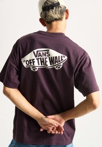 Camiseta de algodón morada con un gran gráfico blanco "VANS 'OFF THE WALL'" en la parte posterior, mangas cortas y un corte relajado.
