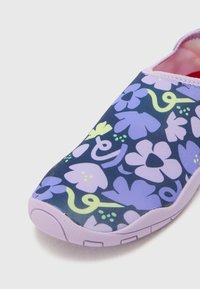 Schoenen met een marineblauwe basis, voorzien van een bloemenpatroon in paars, groen en geel. De zool is lila en het ontwerp heeft een gladde, flexibele textuur.