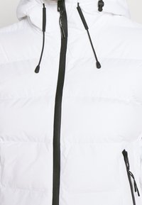 Hvid dunjakke med lynlås foran, sorte detaljer og justerbare snore. Har en quiltet tekstur og sidelommer.