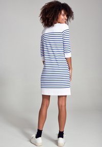 Abito a righe bianco e blu, con scollo a barca, maniche a tre quarti e taglio dritto, abbinato a sneakers bianche.