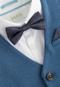 Blazer bleu tissé avec une finition texturée, chemise blanche à boutons et nœud papillon bleu marine avec un motif géométrique.