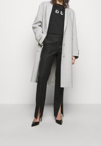 Grijs geruit overjas, zwart t-shirt met witte opdruk, zwarte op maat gemaakte broek met zijsplitten en zwarte puntige hakken.