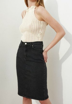 Kremowy, dziergany top bez rękawów o prążkowanej fakturze i wysokim kołnierzu, zestawiony z czarną spódnicą midi z denimu z rozporkiem z przodu i bocznymi kieszeniami.