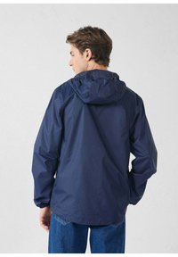 Giacca impermeabile blu navy con cappuccio, polsini elastici e vestibilità comoda, realizzata in materiale liscio e leggero. Design senza cuciture sulle spalle.