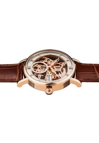 Orologio scheletro con cassa in oro rosa, vetro trasparente e cinturino in pelle marrone. Ingranaggi esposti e dettagli intricati visibili attraverso il quadrante.