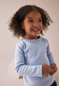 Hellblaues Langarmshirt mit gerafftem Ausschnitt und einer kleinen Schleife als Akzent, mit einem strukturierten Stoffmuster.