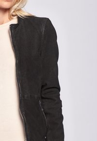 Svart perforerad läderjacka med en figursydd design, som har en dragkedjestängning fram och ribbad textur längs ärmarna.