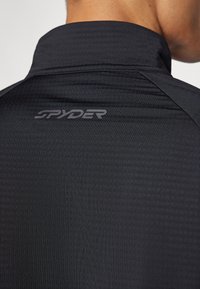 Schwarzes Sportshirt mit Stehkragen und strukturiertem Stoff, mit einem grauen "SPYDER"-Logo auf dem Rücken.