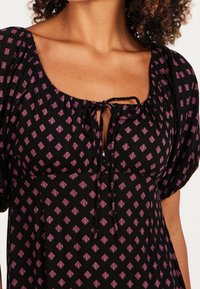 Svart klänning med korta puffärmar och rundad halsringning. Har en knytdetalj och ett diamantmönster i rosa nyanser över tyget.