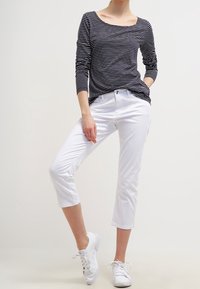 Granatowo-biały top w paski z długim rękawem i dekoltem w łódkę, zestawiony z białymi spodniami 7/8 i białymi trampkami.