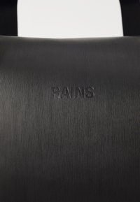 Čierna taška s textúrovaným povrchom, na ktorom sú horizontálne prúžky a vyrazené logo "RAINS", navrhnutá s minimalistickou estetikou a odolnosťou.