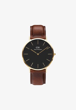 Orologio con quadrante nero e cassa in tonalità oro, con indicatori delle ore allungati e cinturino in pelle marrone. Design minimalista con lancette semplici. Accenti in ottone.