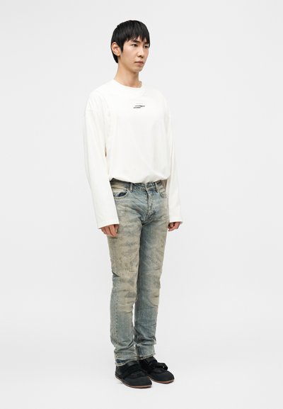 Valge pikal varrukal särgiga, millel on väike silt, helesinised kulunud teksad tuhmunud mustriga ja mustad kingad, millel on kaks rihma.