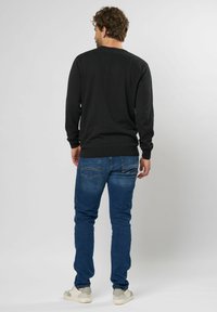 Schwarzes Langarmshirt mit gerippten Bündchen und Saum, kombiniert mit blauen Slim-Fit-Jeans, getragen mit hellen Sportschuhen.