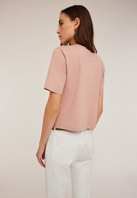Tricou scurt, de culoare roz deschis, cu mâneci scurte, textură fină, guler rotund și croială lejeră, asortat cu pantaloni albi cu talie înaltă.